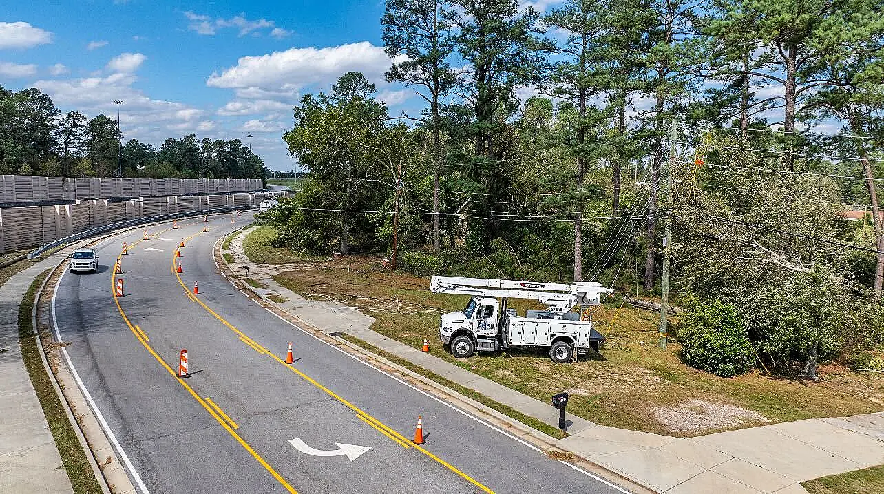 Utility truck parked near a wooded area beside a curved road.